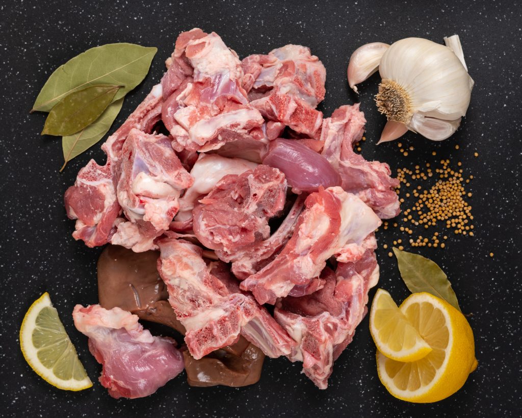 Fresh raw goat meat stew like cuts on black cutting board with spices (mustard seeds, garlic, lemon, and bay leaves).