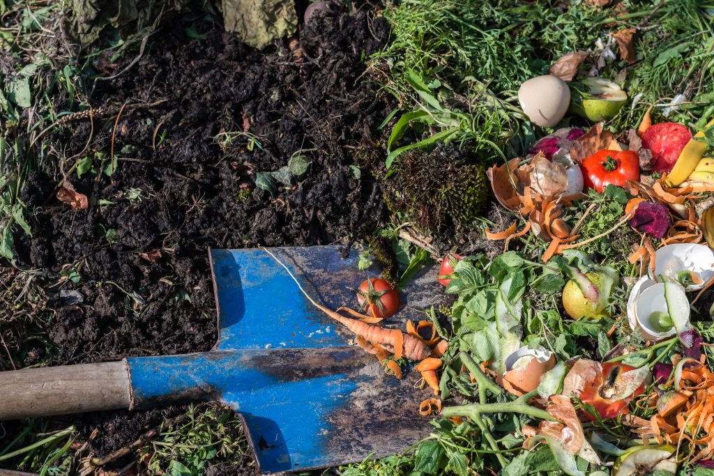 Compost box outdoors full with garden browns and greens and food  wastes, blue shovel in the soil, sustainable life concept