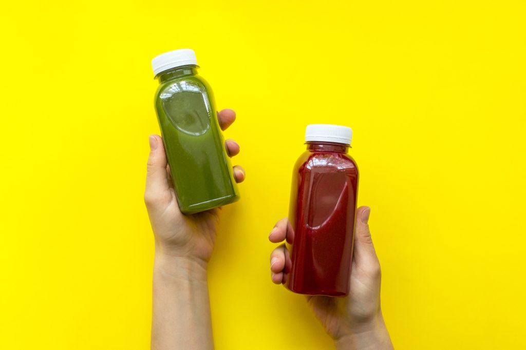 Female hand holding plastic bottles with juice or smoothie on yellow background. The concept of diets, detox
