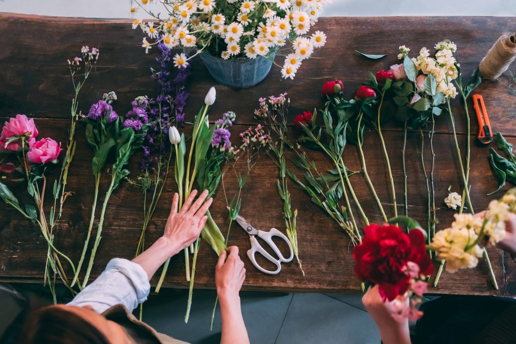 Florist makes a trendy modern bouquet of different flowers on a wooden table background. View from above