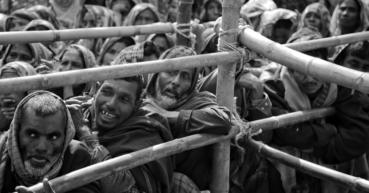 a black and white image of a crowd waiting behind a bamboo fence illustrating patience and resilien