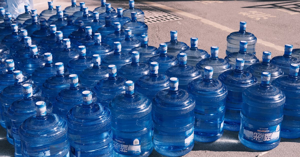 a collection of blue plastic water jugs lined up on an urban street in sunlight