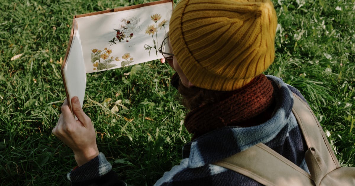 a person wearing a beanie examines a botanical sketchbook in a grassy field