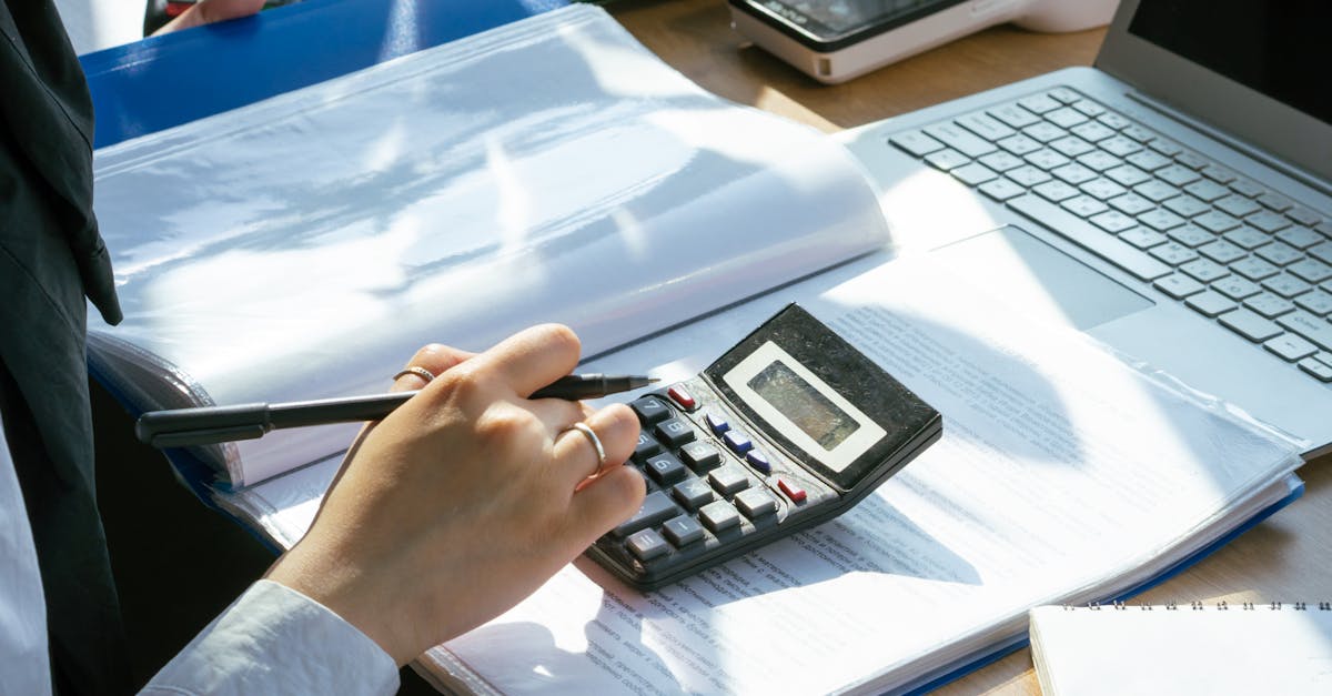 a person working on financial calculations using a calculator and laptop at an office desk