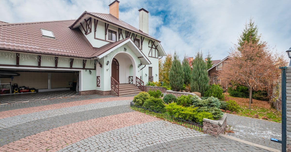 a quaint suburban house with a beautiful garden and brick driveway under a partly cloudy sky