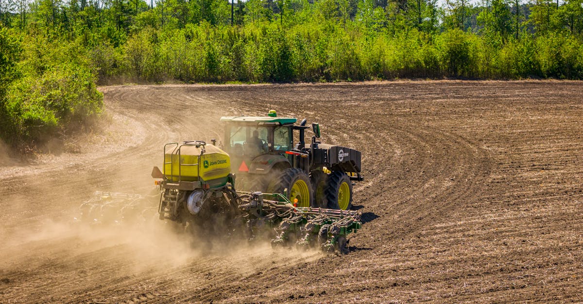 a tractor tills a vast field in rural north carolina surrounded by dense greenery
