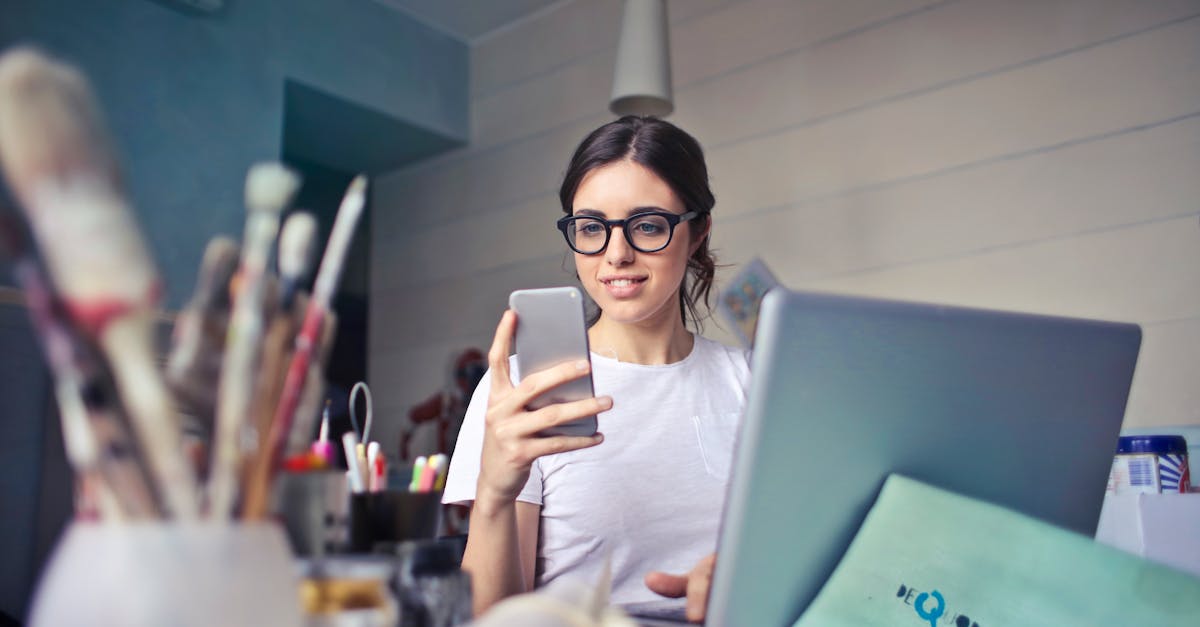 a woman using her phone at a desk surrounded by art supplies and a laptop in a creative workspace 1