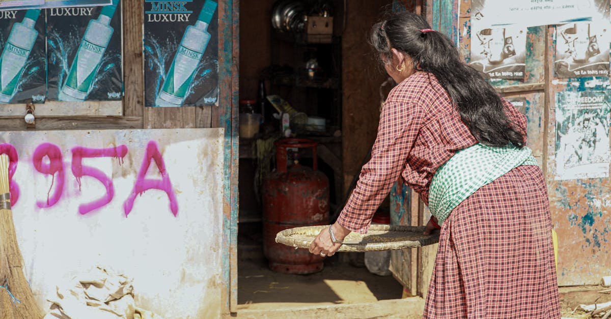 a woman winnowing grains outside a rustic graffiti marked house