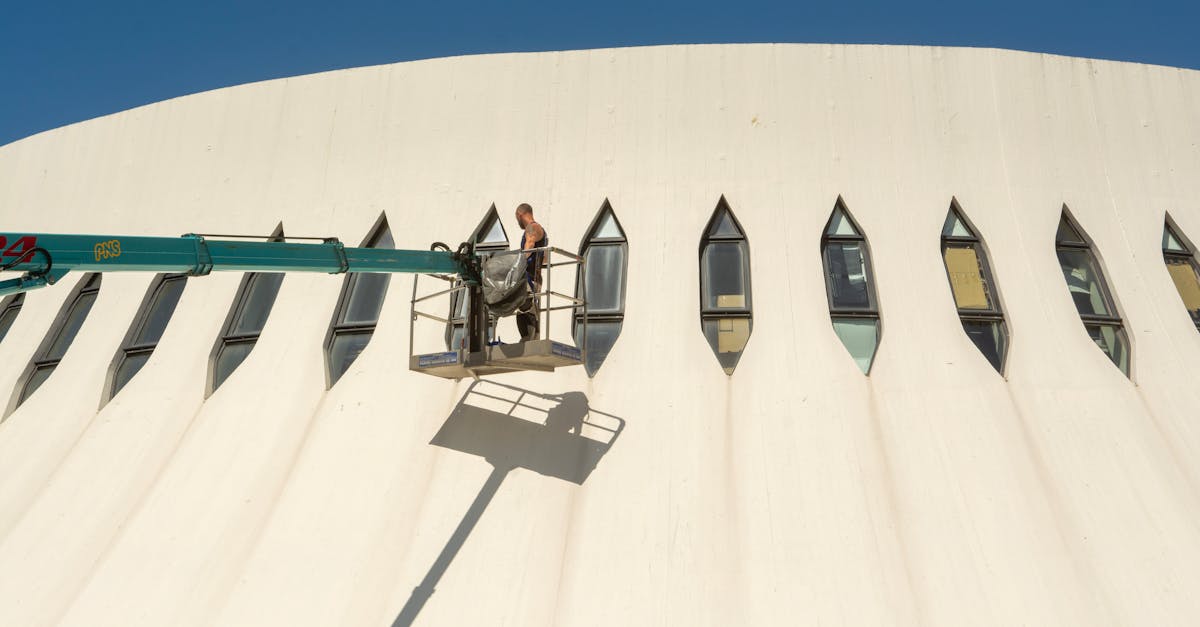 a worker on a lift maintaining the unique facade of a modern building under clear skies