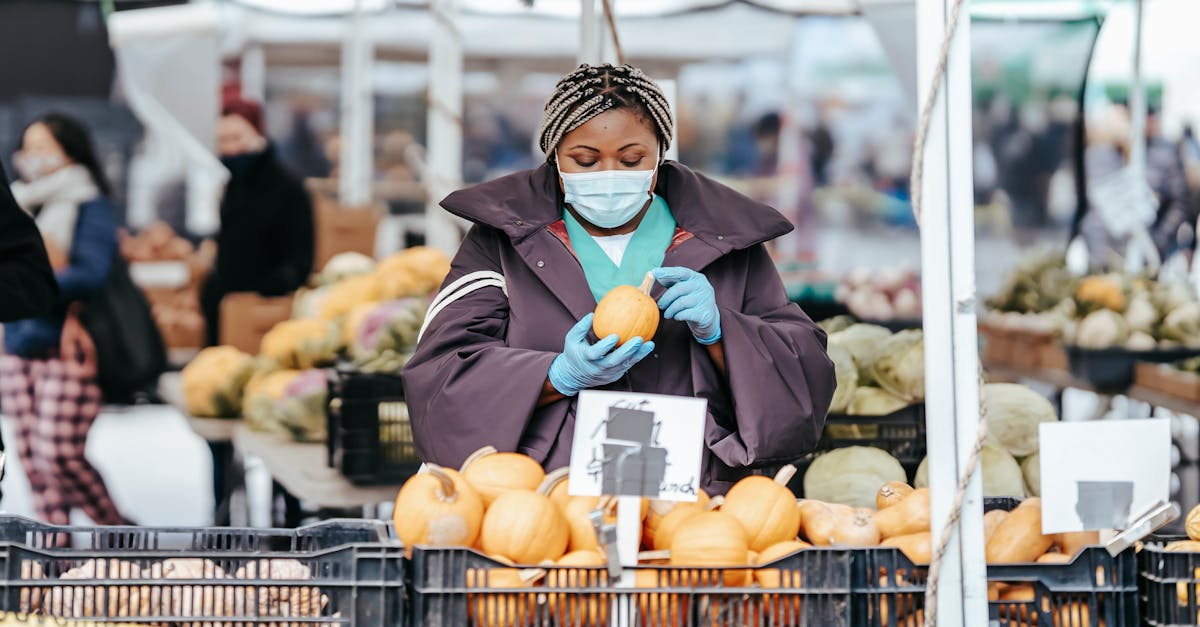 adult african american female nurse in medical uniform and gloves with mask choosing pumpkin from bo