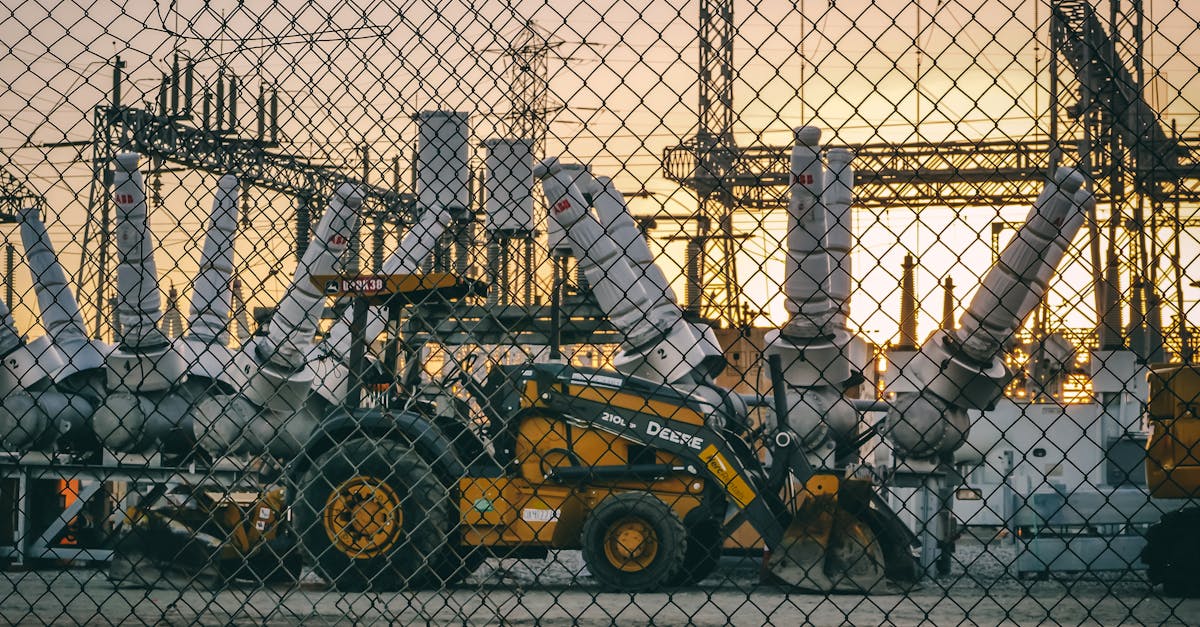 an industrial power plant with heavy machinery and equipment behind a chain link fence during sunset