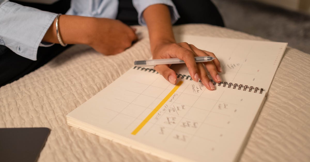 close up of a person scheduling in a spiral bound planner using a pen indoor setting