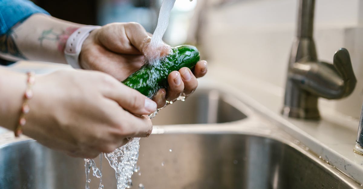 close up of hands washing a green vegetable under a kitchen faucet emphasizing cleanliness and food