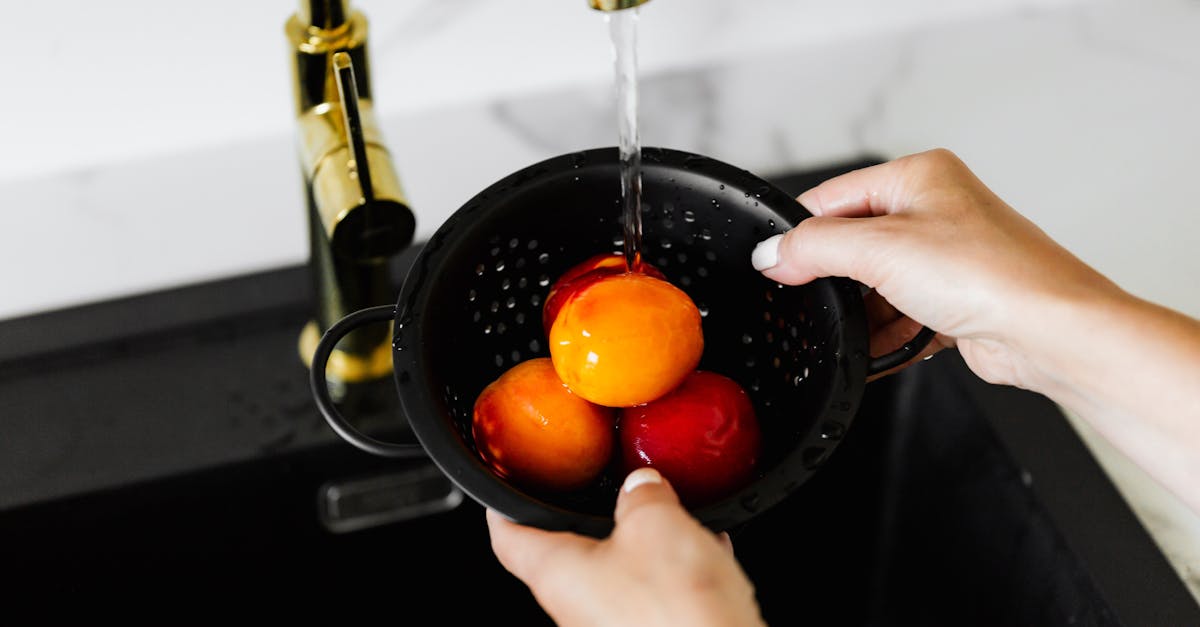 close up of hands washing ripe peaches in a kitchen under a running tap 1