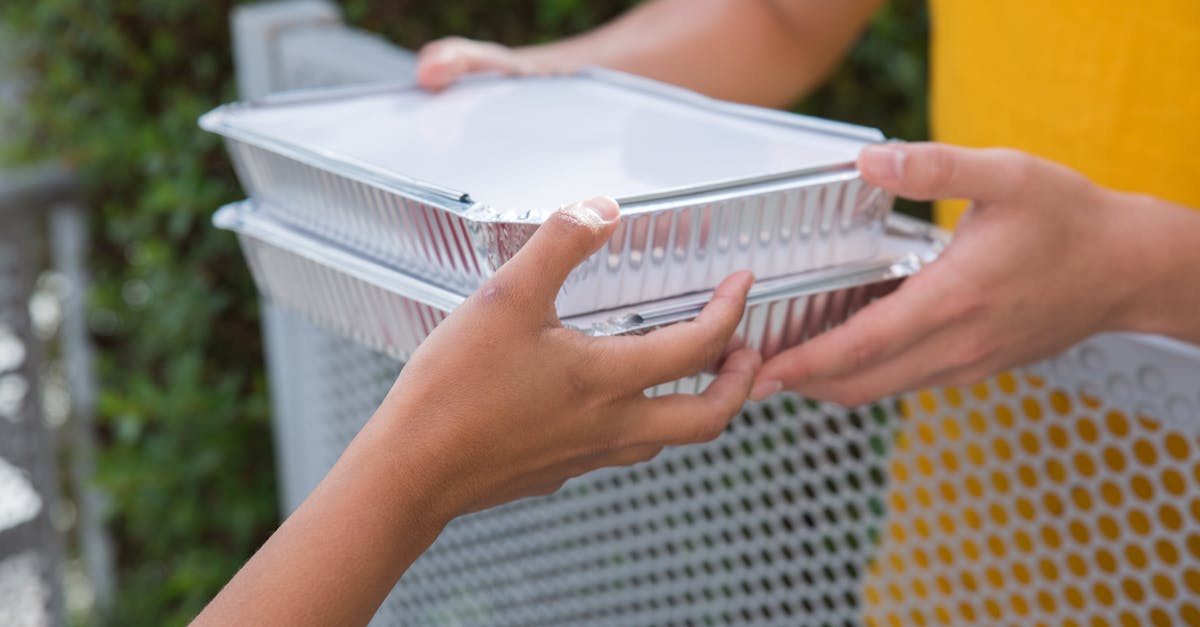 close up of two people exchanging aluminum food containers over a metallic fence outdoors 6