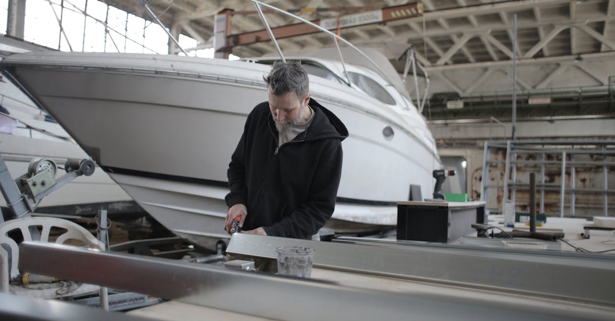 concentrated bearded adult workman in casual wear working with metal detail near boat in garage
