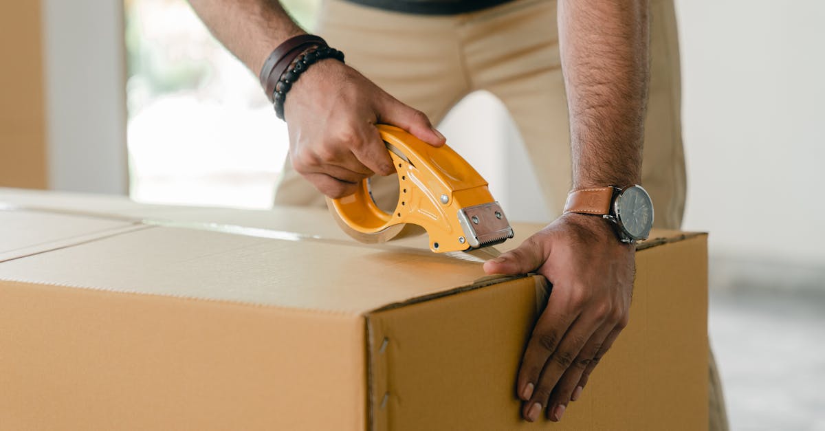 crop faceless young male with wristwatch using adhesive tape while preparing cardboard box for trans
