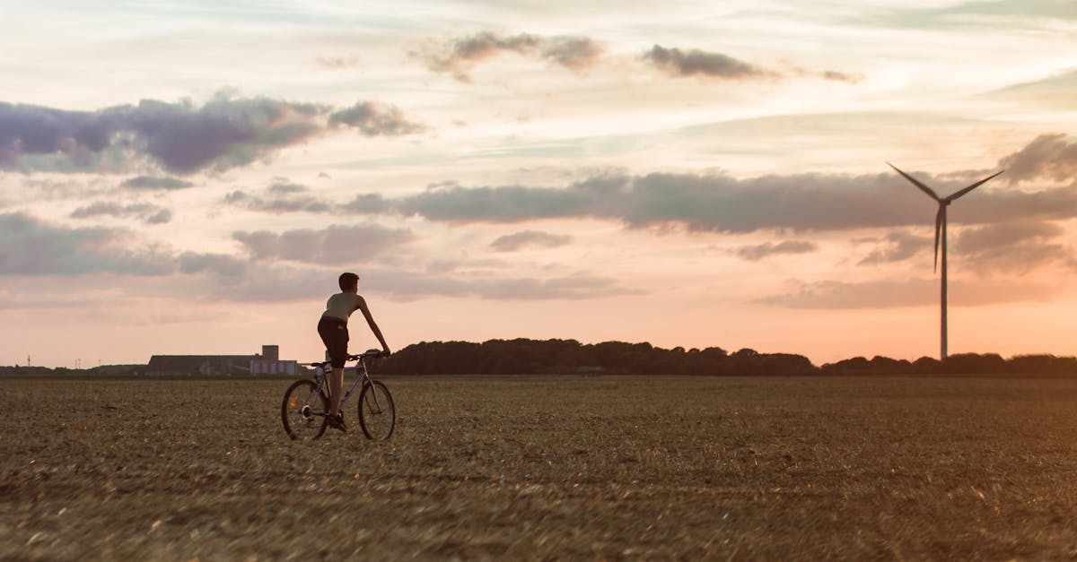 cyclist rides through field with wind turbine at sunset symbolizing renewable energy 2