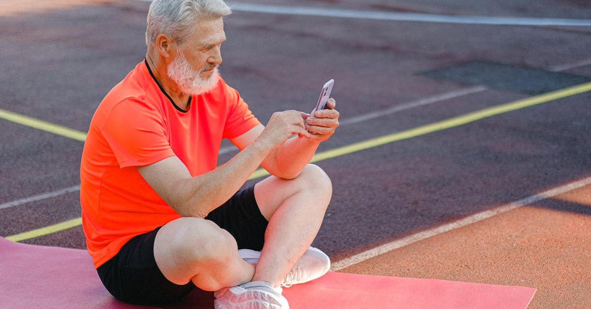full body of focused senior male athlete in sportswear sitting on stadium and browsing mobile phone