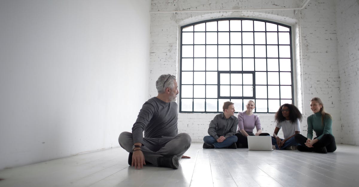 full body of positive multiracial colleagues in casual clothes sitting in lotus pose on floor while