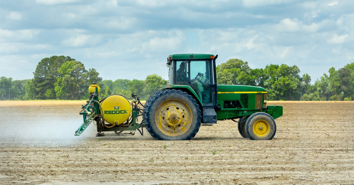 green tractor with sprayer working in an open farm field under a cloudy sky