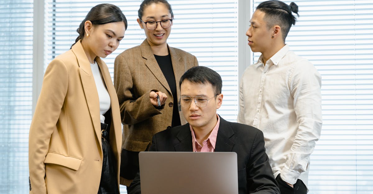 group of colleagues in formal wear actively discussing work around a laptop in office setting