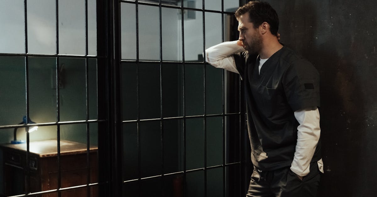 man in uniform stands pensively by barred prison wall illuminated by dim light