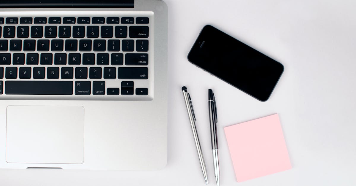 overhead view of a sleek workspace featuring a laptop smartphone and stationeries on a white desk