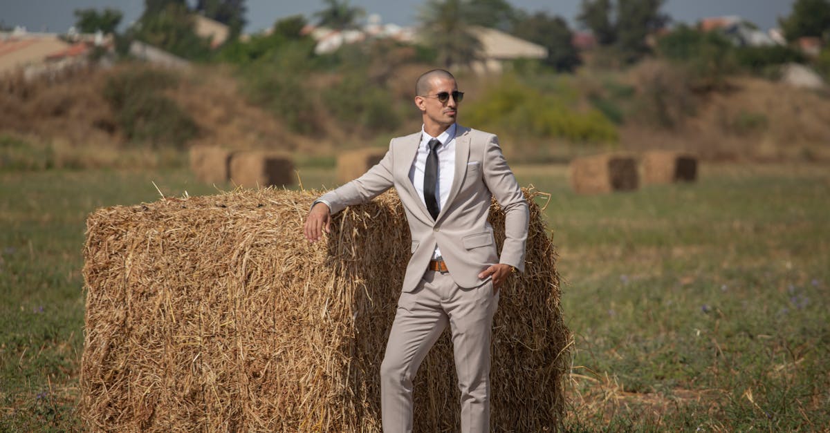 professional businessman in a suit leans casually on a hay bale in a countryside setting