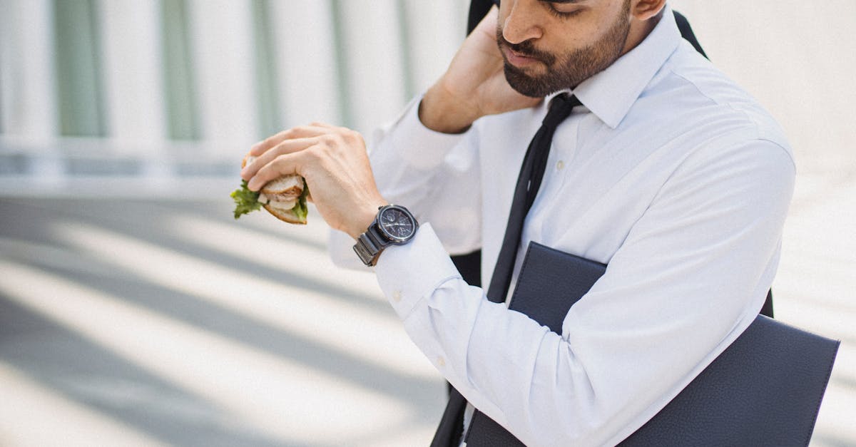 professional man in corporate attire checking time while holding a sandwich outdoors