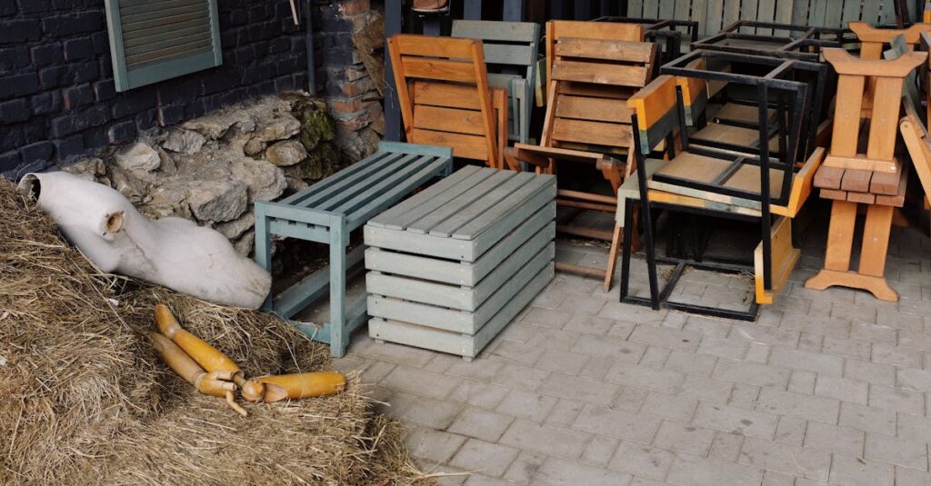 stacked wooden furniture and straw bales outdoors against a stone wall creating a rustic scene