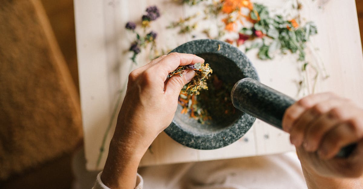 top view of hands grinding dried herbs using a mortar and pestle on a wooden table