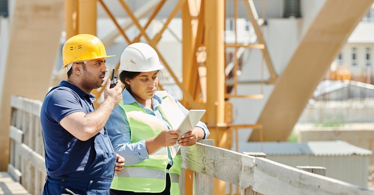 two construction workers in hardhats discuss plans using a tablet and walkie talkie on site