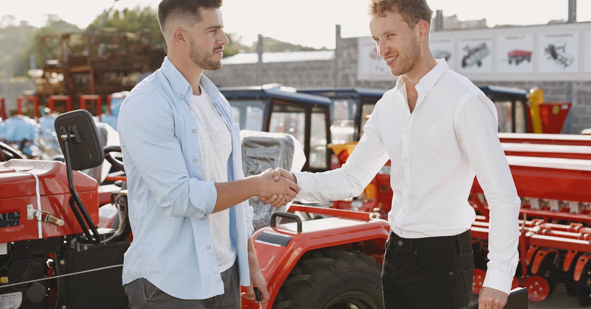 two men shaking hands near a tractor symbolizing a business deal or purchase agreement outdoors