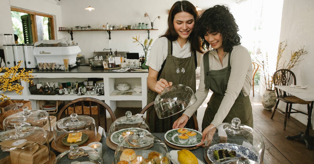 young smiling waitresses in aprons preparing delicious desserts for tea time in small cafe