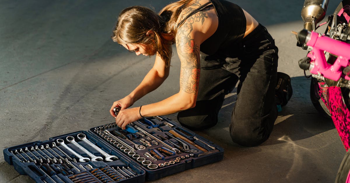young tattooed woman in black tank top organizing tools from a toolbox beside a motorcycle