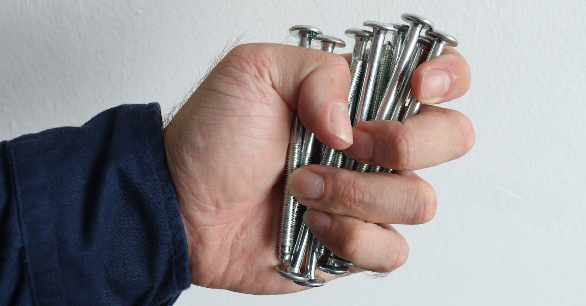 a detailed image of a hand tightly gripping shiny metal screws against a white background