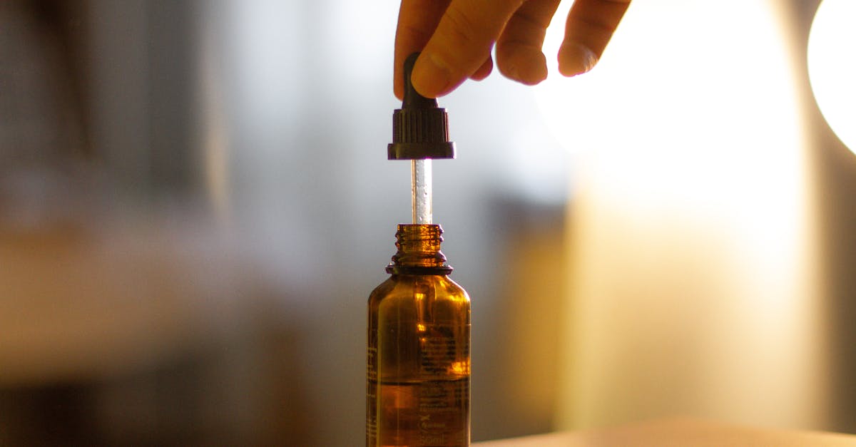 a hand holding a serum dropper over a brown glass bottle with a blurred background
