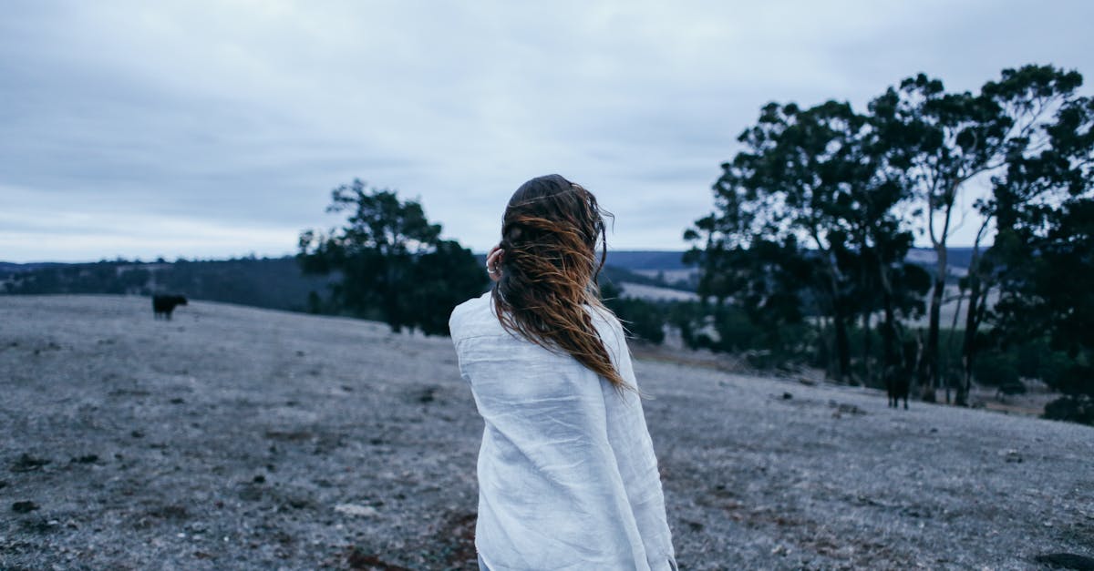 a woman in a white shirt explores a vast open field under a cloudy sky embracing nature s serenity
