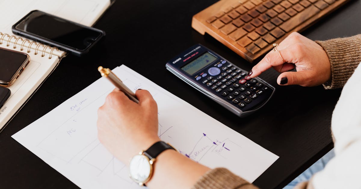close up of hands working with a calculator and notebook on a desk analyzing documents