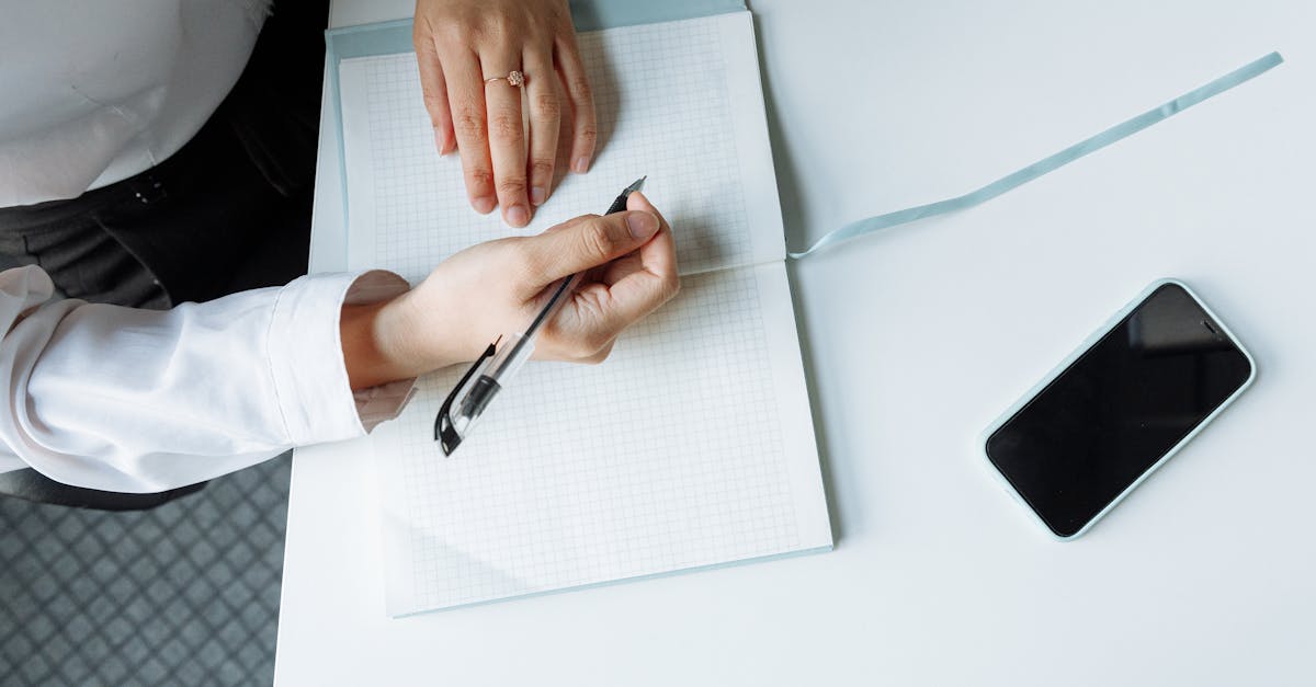 close up of hands writing in a notebook with a smartphone on a white desk
