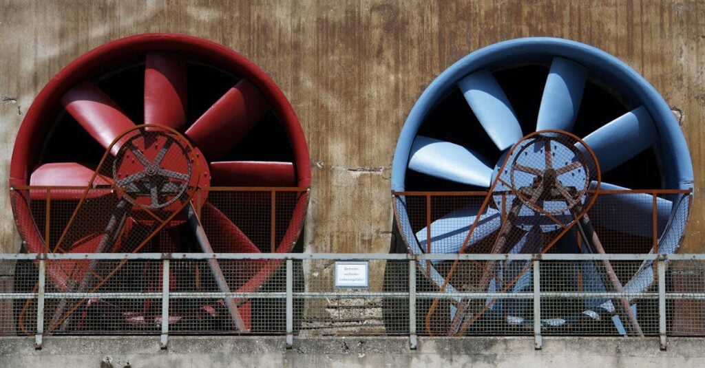 close up of large red and blue industrial fans on a rustic wall showcasing machinery and ventilation