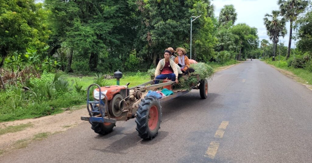 farmers riding a vintage tractor loaded with greens on a rural road in cambodia