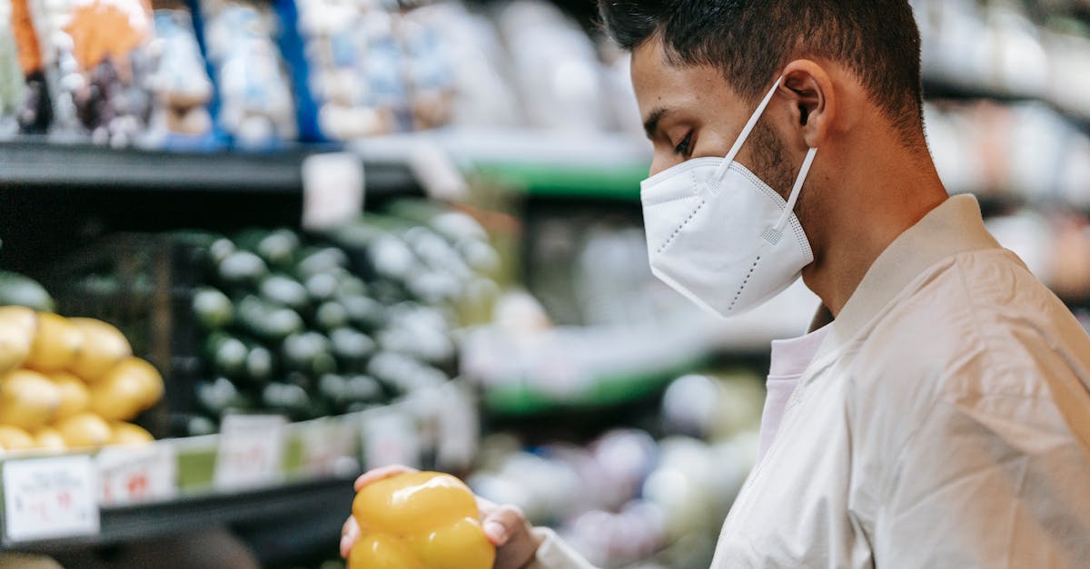 side view of indian male buyer in medical mask standing with yellow bell pepper in hand near stall w