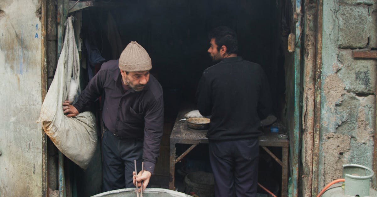 two men cooking in a rustic outdoor kitchen with gas tanks and metal tools