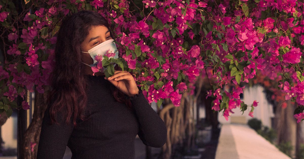 woman in face mask surrounded by vibrant pink bougainvillea flowers in a garden setting