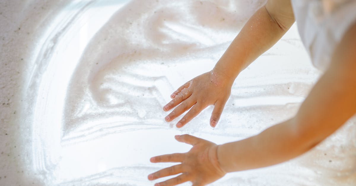 a child happily plays with foamy substance using hands on a light surface