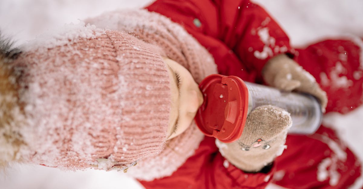 a child in snow proof clothes enjoys a drink from a tumbler in a snowy outdoor setting 1