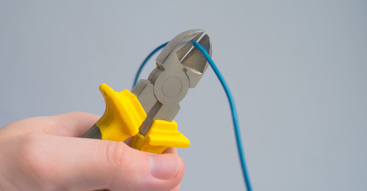 a close up image of a hand using pliers to cut a blue wire against a gray background