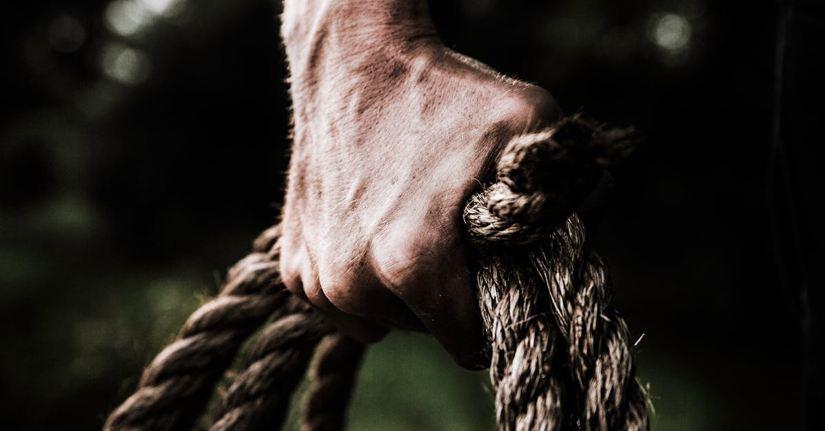 a close up image shows a strong firm hand gripping a thick rough rope showcasing strength and det